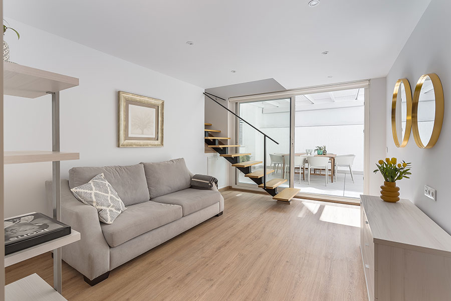 View of the living room with wooden staircase and patio in the background in the 4-bedroom duplex rental flat in Cuatro Caminos, Madrid.